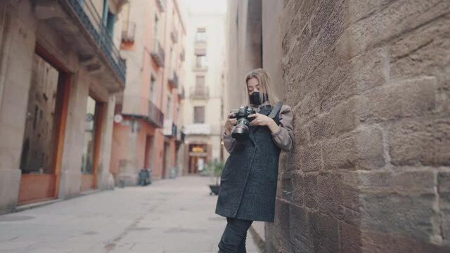 tourist woman wearing mask with dslr photo camera walking through old town narrow streets, Barcelona, Spain. She takes photos. covid tourism concept with coronavirus. Prores 10 bit