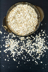 Dry oatmeal porridge in a transparent bowl on a dark background close-up, top view. Vertical photo