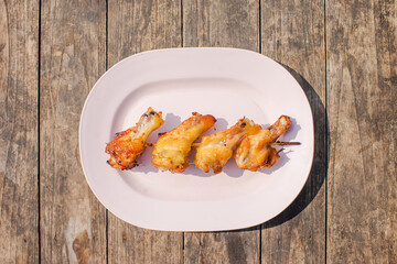 Grilled chicken legs put on a pink plate on a wooden table.