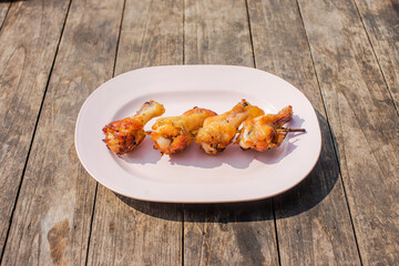 Grilled chicken legs put on a pink plate on a wooden table.