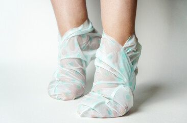 the girl puts on a moisturizing foot mask, for dry heels of the feet. Woman wearing disposable moisturizing socks for the legs on a white background