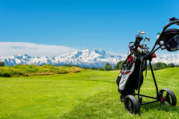 Golf cart with bag and golf clubs at the edge of the fairway of a golf course. In the background the Alps, the Monte Rosa chain, seen from the Italian side.