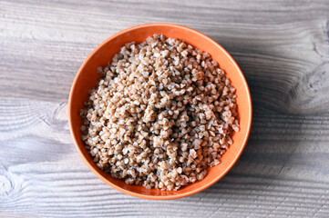 Buckwheat porridge in an orange ceramic plate on a wooden table. Top view. Image with selective focus.