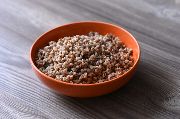 Orange ceramic plate with buckwheat porridge on a wooden table. Image with selective focus.