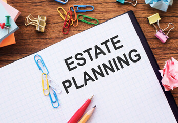 Notebook with text ESTATE PLANNING on a table with sticks, colored paper clips and wrinkled sheets.