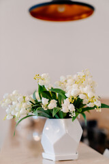 small white vase with lilies of valley on table under black copper chandelier.