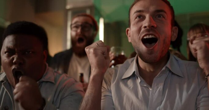 Focus on handsome man looking excited and rejoicing while supporting favourite team. Guy and his multiethnic diverse friends becoming happy while watching sports game in beer pub