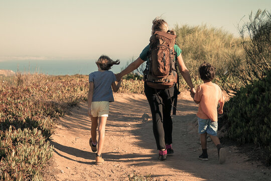 Mom And Two Kids Hiking Outdoors, Walking On Countryside Path. Back View. Nature And Recreation Concept