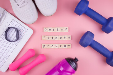 Online fitness program. Sneakers, laptop, fitness bracelet, water bottle and dumbbells, on a pink background, workout online.
