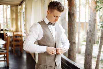 happy gorgeous handsome groom getting ready dressed in the morning. The groom puts on a suit for the wedding preparing for the holiday