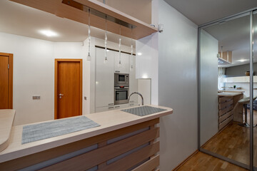 Modern interior of kitchen in luxury flat New kitchen set with light wooden counter. Wooden doors. Mirror sliding door.