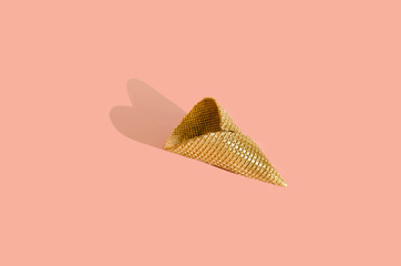 Golden ice cream cone with heart shaped shadow on powder pink background. Minimal Concept