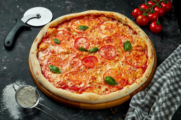 Appetizing Italian pizza with cheese, tomatoes, basil and red sauce in a composition with ingredients on a black background. Pizza margarita