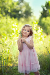 a girl in a pink dress stands in a field on the grass on a summer day