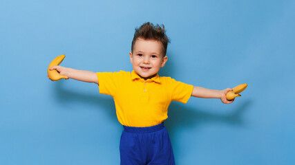 A boy in a yellow T-shirt is holding a banana with a smile. Funny expressions. The concept of nutrition. Fresh banana. Yellow style. Blue background