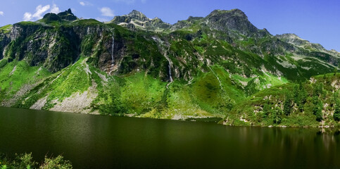 Fototapeta na wymiar rocky mountains with waterfalls and green plants at a lake panorama