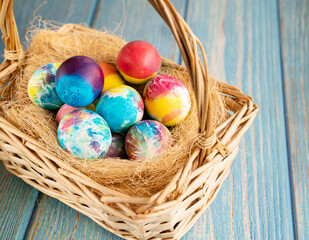 Easter decorated eggs in a basket on the hay on turquoise wooden background.