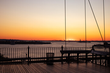 Obraz premium Beautiful Sunset on the East River in New York City with the Silhouette of the Statue of Liberty in the Distance seen from the Brooklyn Bridge