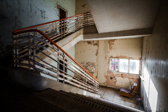 Abandoned Building Creepy Dark Moody Staircase In Dilapidated Run Down Old Deserted Hospital School Ruin With A Single Empty Chair Indoors On Stairs Landing No One There