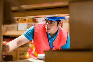 Asian male worker with safety vest and helmet using clipboard for checking products shelf pallet in...