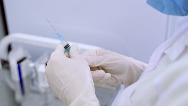 The nurse draws the vaccine into a syringe. Nurse's hands in white rubber gloves