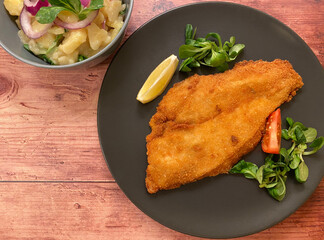 Golden breaded fish plaice fillet with potato salad and lemon.