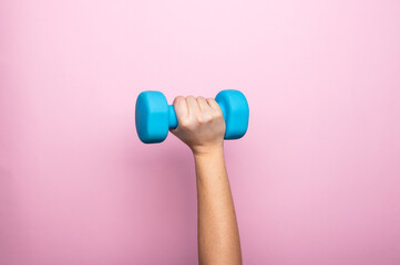 Woman's hand holding blue dumbbell isolated on pink background. Home workout, fitness, and activity. Sport and healthy lifestyle concept with copy space.