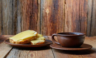 A cup of coffee and toast with melted cheese on a plate, sitting on a wooden table. On an old country background.