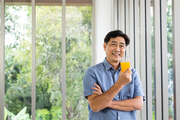 Active senior Asian man smile while holding and drink organic orange juice for breakfast. Healthy...
