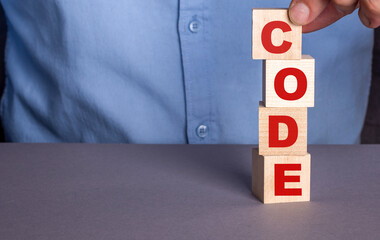 A man in a blue shirt composes the word CODE from wooden cubes vertically