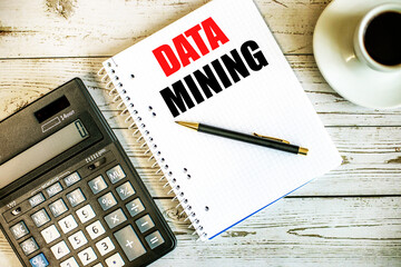DATA MINING written on white paper near coffee and calculator on a light wooden table. Business concept