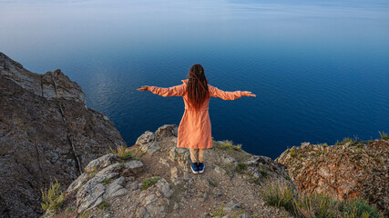 Girl with opened arms on the edge of the cliff lookind at the sea
