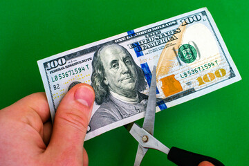 a man cuts a hundred-dollar bill with scissors