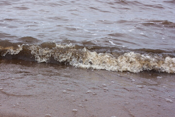 a light wave rolls over the sandy shore, a cloudy day