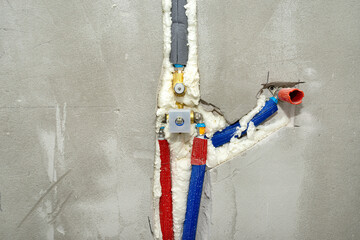 A brass tap inserted into the plaster in a concealed shower, insulated water pipes visible.