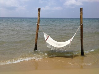 White textile hammock on woodem poles in the beach, in the water