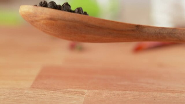 Black Peppercorn Spices on Wooden Teaspoon Falling onto Tabletop in Slow Motion