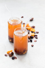 Compote of dried fruits, dates, dried apricots, cranberry,  raisins in a glass jar with a straw on a light gray background