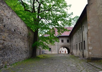 passage between monastic buildings arch stone wall green tree red monastery slovakia spring