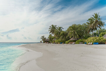 Traumhafter Strand mit Palmen und Sonnenliegen auf einer kleinen Insel auf den Malediven, im Hintergrund blauer Himmel