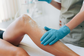 Cosmetologist is sprinkling and distributing talcum powder on a young girl's leg before the epilation procedure. The girl is lying on a couch in a beauty salon, she does the procedure shugaring