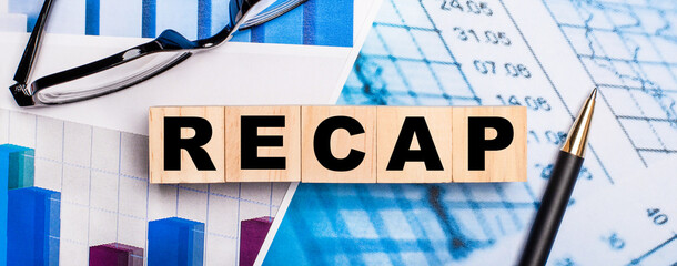 On the bright diagrams, glasses, a pen and wooden cubes with the word RECAP. Business concept