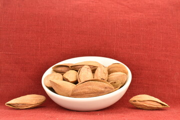 Unpeeled organic dried almonds in a ceramic bowl, close-up, on the background of a red linen napkin.