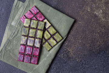 Two bars of natural festive vegan chocolate with a bright colored glaze in pink and green, on a purple background. The concept of the holiday. Copy space