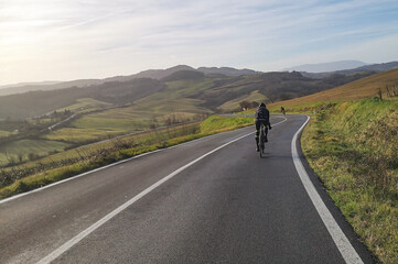 Fototapeta na wymiar ciclista fa sport pedalando lungo una strada nella campagna collinare toscana