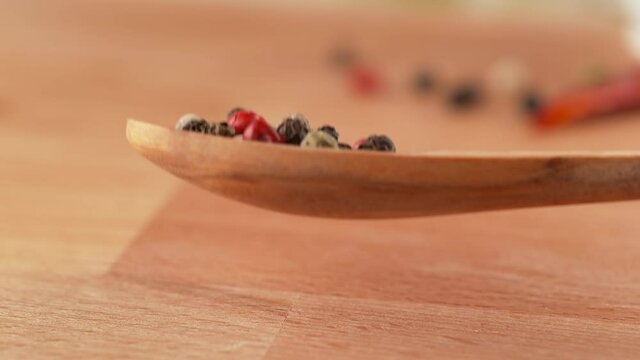 Colorful Peppercorn Blend on Wooden Teaspoon Falling onto Tabletop in Slow Motion
