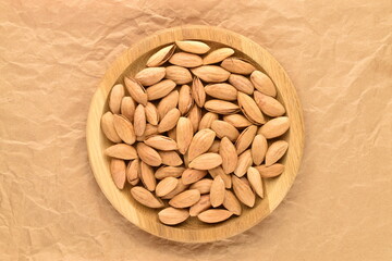 Unpeeled organic dried almonds in a wooden plate, close-up, on brown paper, top view.