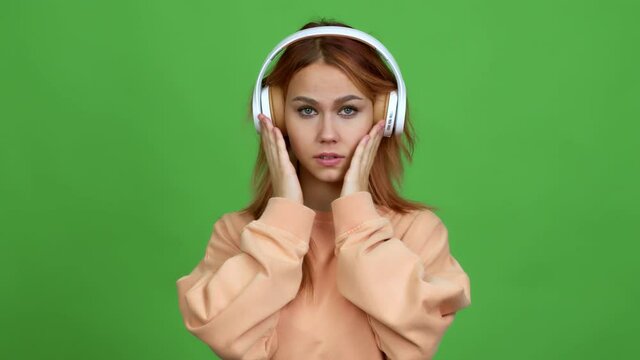 Teenager girl listening music with headphones covering mouth with hands. Can not speak over isolated background