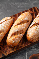 Three loafs of fresh baked baguette on the wooden cutting board on gray background