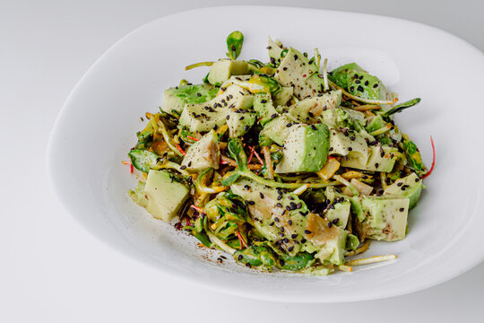 Fresh mix salad with avocado and sauce on a concrete background. Organic healthy salad of iceberg, avocado and cucumber with olive oil and sesame seeds. Healthy green salad with microgreen. 